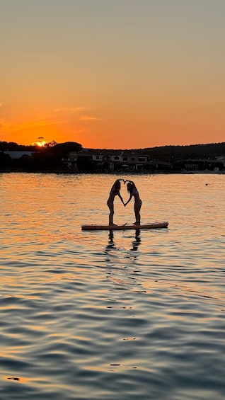 Two people forming a heart shape with their hands on a paddleboard in calm water during sunset. 5