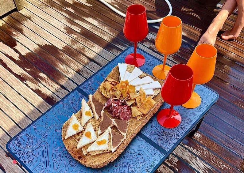 A wooden table with a blue tray holding a sandwich, chips, and two glasses of red drink. 3
