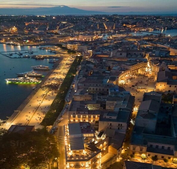 A cityscape at dusk with illuminated buildings, a waterfront, and a busy street. 2