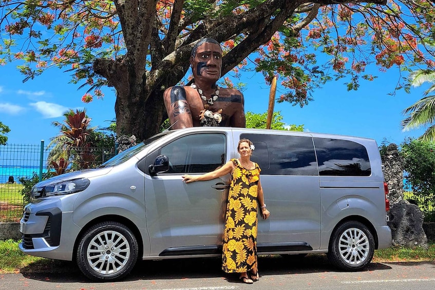 A person standing next to a silver van with a large tree and colorful flowers in the background. 4