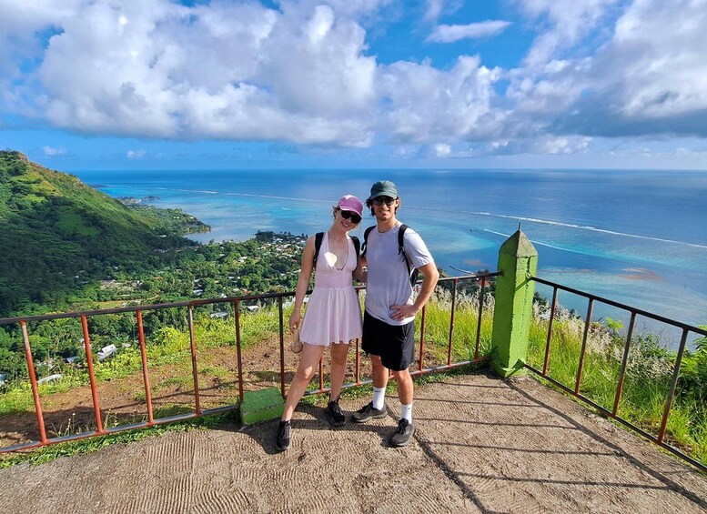A couple standing on a viewing platform with a scenic ocean and hills in the background. 1