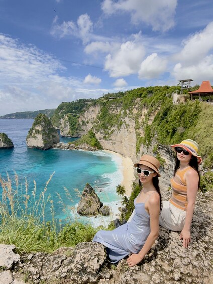 Two people sitting on a rocky outcrop overlooking a coastal landscape with cliffs and a beach. 1