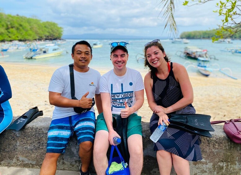 Three people sitting on a stone wall by a beach with boats in the water. 4