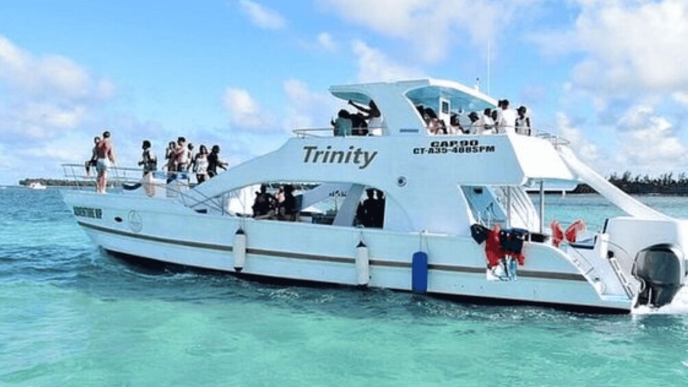 A white boat named 'Trinity' with people on deck and a clear blue sky in the background. 1