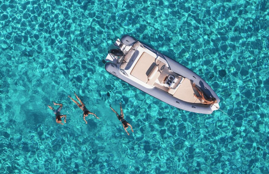 A boat on clear turquoise water with three people swimming nearby. 1