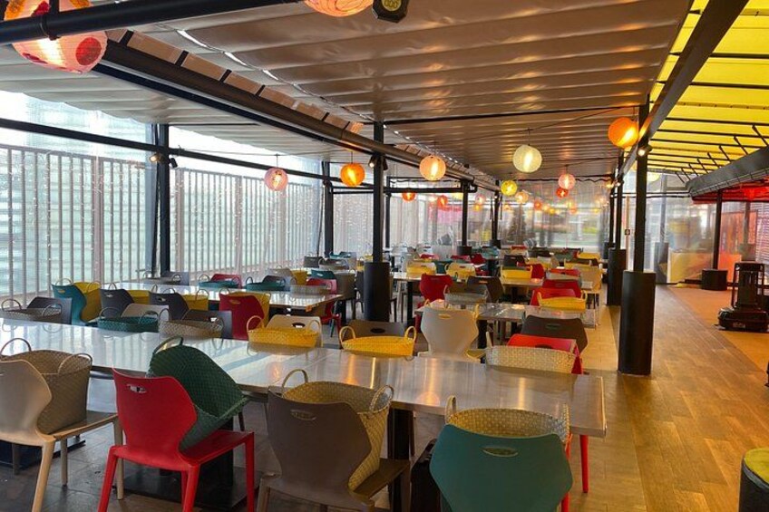 A spacious indoor dining area with colorful chairs and tables, large windows, and hanging lights. 3