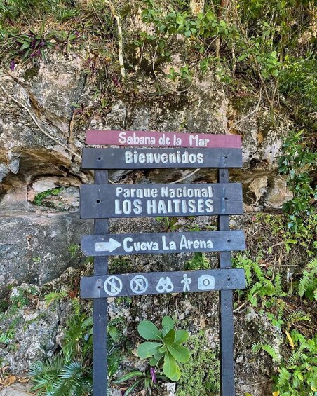 A wooden signpost with directional arrows and symbols indicating park access, a welcome message, and a nearby location named 'Sabana de la Mar.' 2