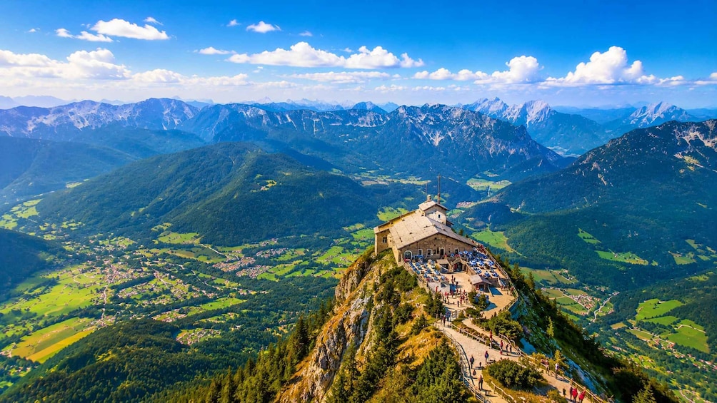 A mountain peak with a chapel and a path leading up to it, surrounded by lush valleys and distant mountain ranges. 1