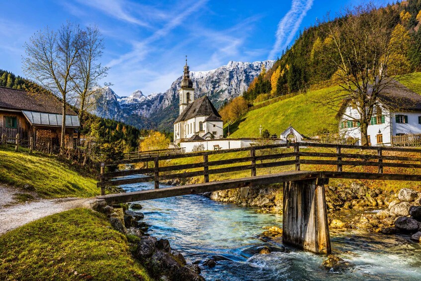A wooden bridge over a river, a church, and mountains in the background. 1