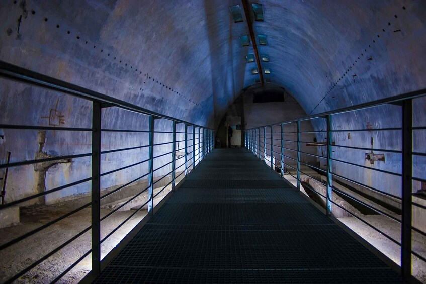 A dimly lit, narrow passageway with metal railings and a tiled floor, leading to a curved ceiling with skylights. 4