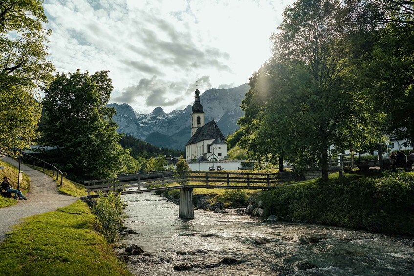 A river, a wooden bridge, a church, and mountains in the background. 2