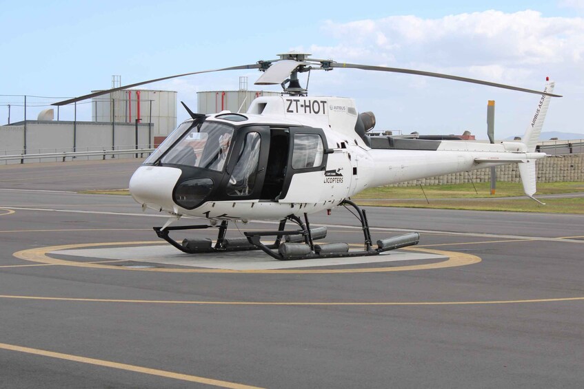 A white helicopter with 'ZTHOT' and 'LICPOTERS' on its side parked on a tarmac with a clear sky in the background. 1
