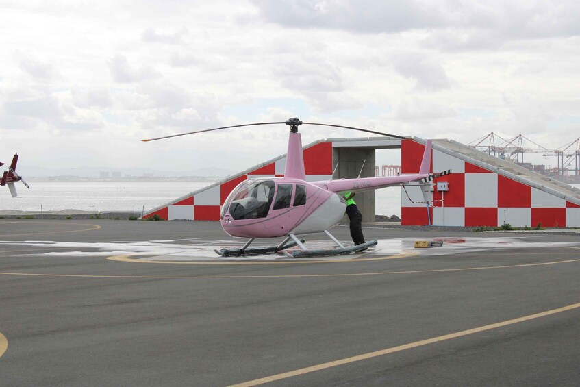 A pink helicopter on a landing pad with a red and white building in the background. 2