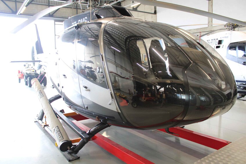 A helicopter with a reflective surface, mounted on a red and white stand, in a hangar with other aircraft in the background. 3