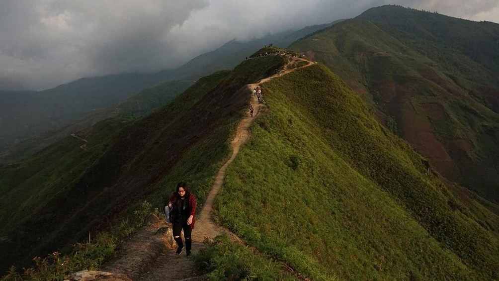 A hiker on a mountain trail surrounded by lush greenery and rolling hills. 4