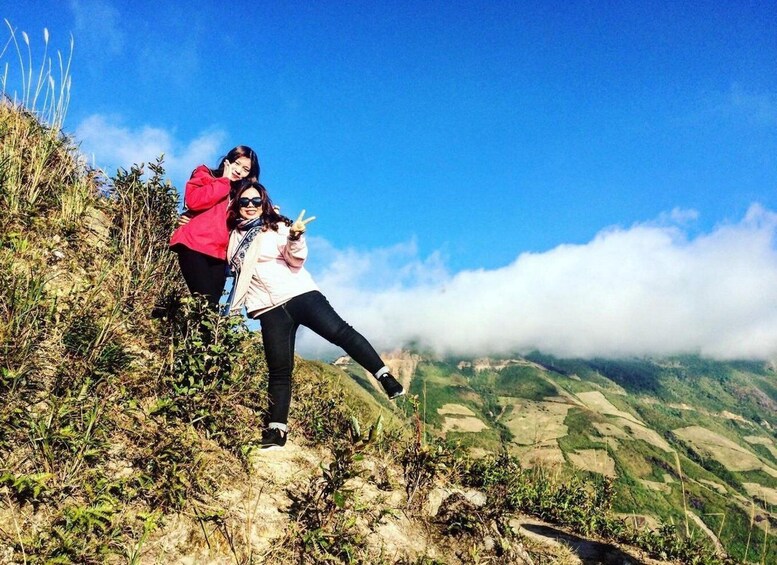 Two people posing on a mountain ridge with a valley and clouds in the background. 2