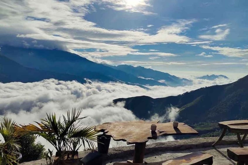 A mountain landscape with clouds below and a wooden table in the foreground. 1