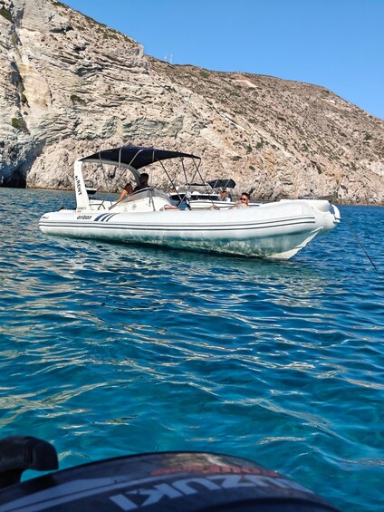 A white boat with 'RENT' written on it, anchored near a rocky coastline. 2