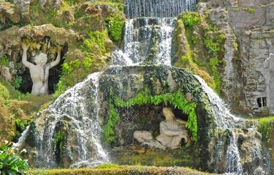 A waterfall cascading over moss-covered rocks with a statue of a figure in the foreground. 4