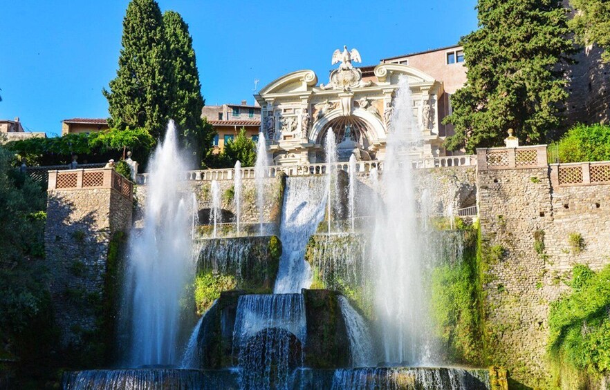 A historic fountain with multiple water jets, a statue, and a classical building in the background. 1