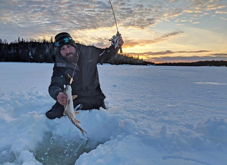 A person kneeling on ice holding a fish. 1