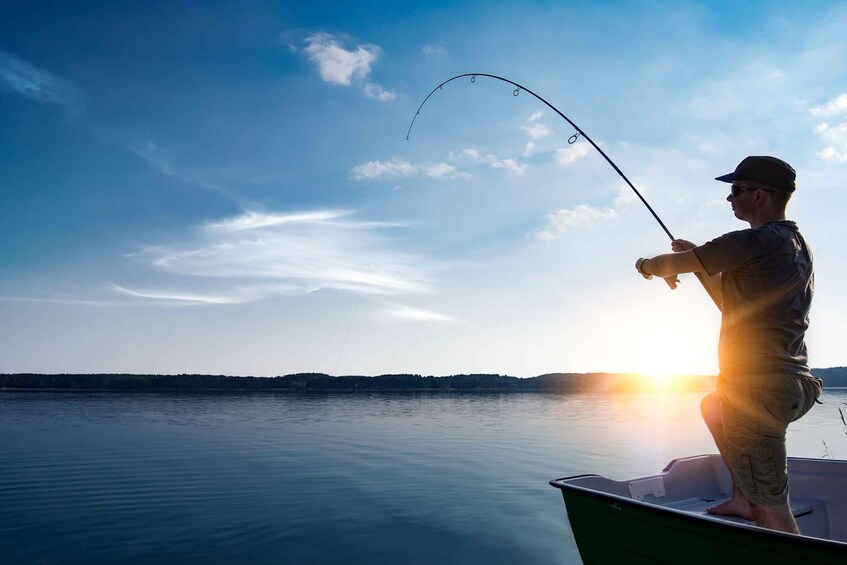 A person fishing on a boat with a calm lake and a sunset in the background. 3