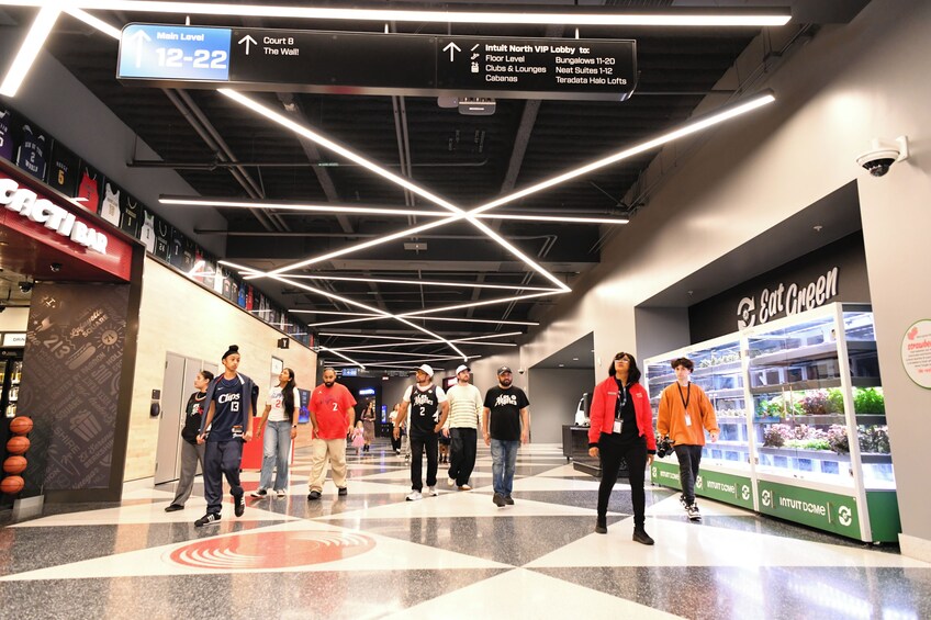 A corridor with directional signs, a basketball court, and a green wall with plants. 2