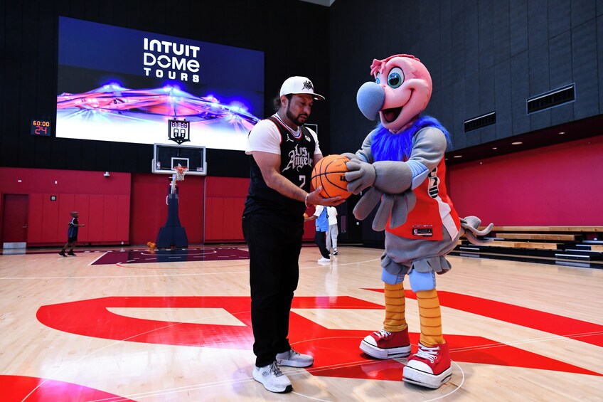 A basketball court with a large screen displaying 'INTUIT DOME TOURS' and a mascot holding a basketball. 3
