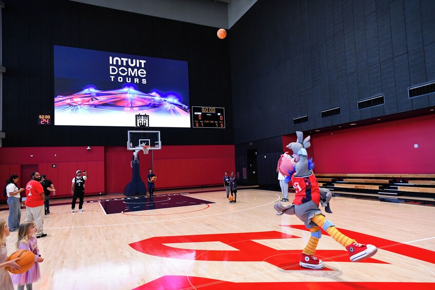 A basketball court with a large screen displaying 'INTUIT DOME TOURS' and a mascot performing. 4