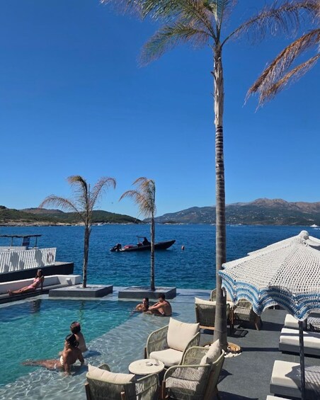 A poolside area with lounge chairs, a palm tree, and a boat on the water. 5