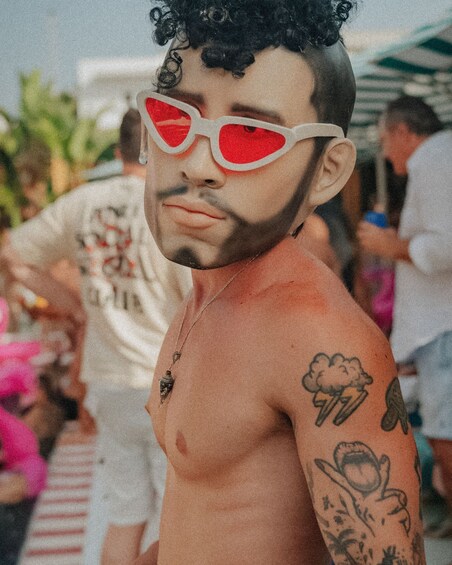A person with tattoos on their arm, wearing a white shirt, and red sunglasses. 3