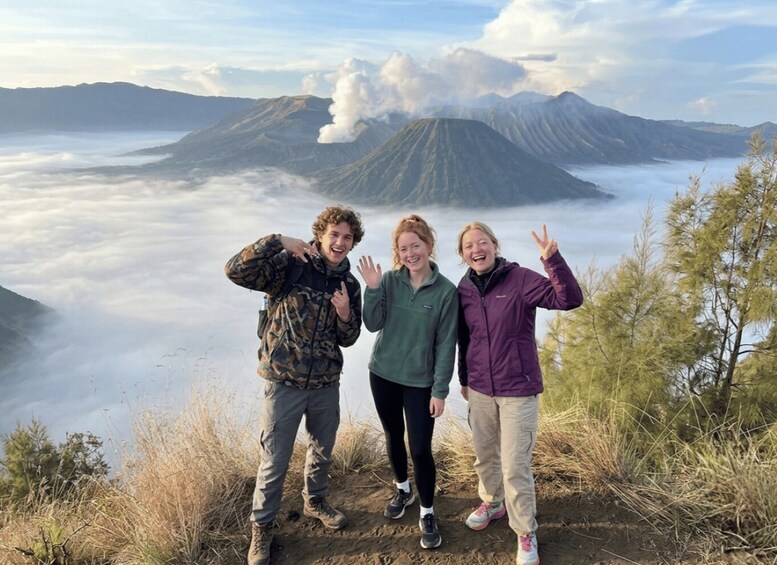 Three people standing on a hill with a volcano in the background. 1