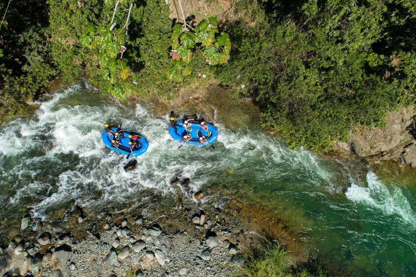 Two blue inflatable rafts navigating a fast-flowing river surrounded by dense green foliage. 2