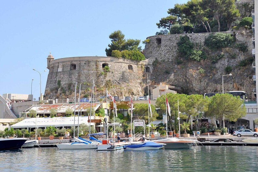 A coastal town with a historic stone fort, marina with boats, and buildings with outdoor seating. 5