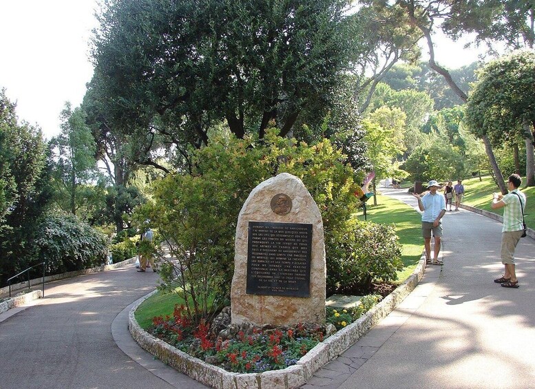 A stone monument with an inscription surrounded by a flower bed and trees. 5
