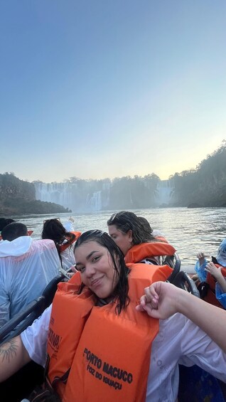A group of people on a boat with life jackets, facing a waterfall. 5