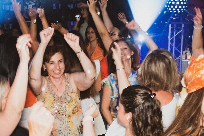A group of people dancing at a party with raised hands and a stage in the background. 2