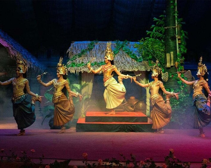 A traditional dance performance on a stage with a thatched-roof backdrop. 1