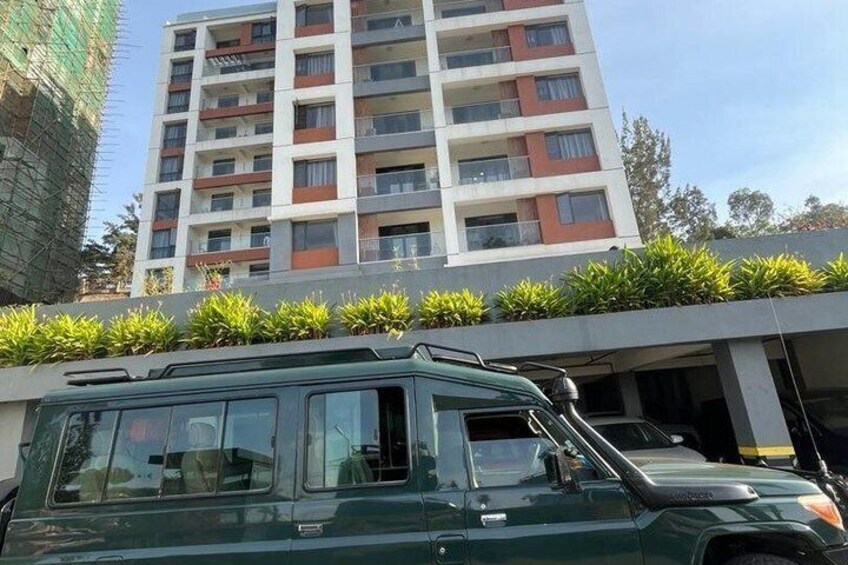 A green SUV parked in front of a modern apartment building with a balcony and a construction site to the left. 5