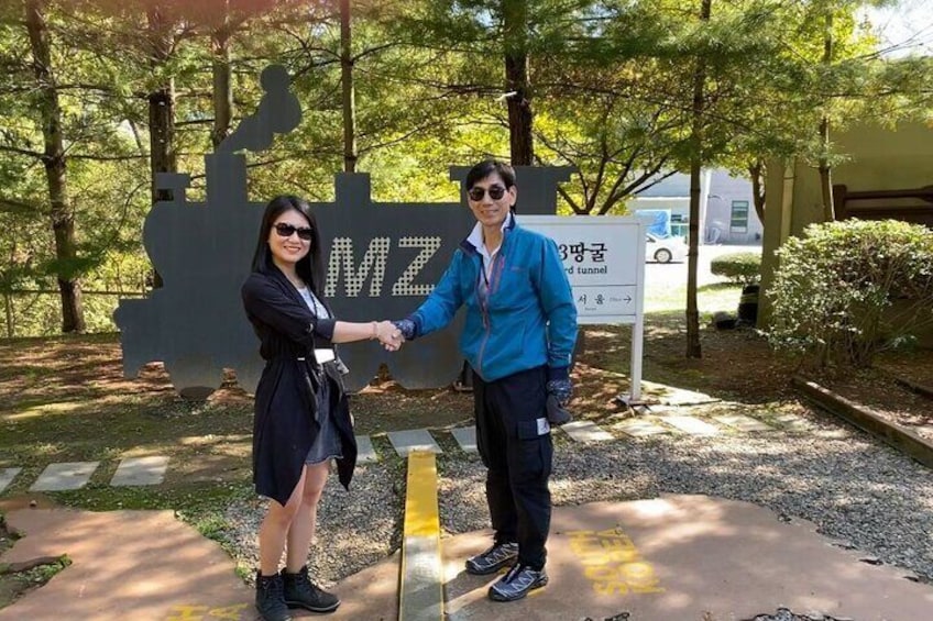 Two people shaking hands in front of a sign with 'MZ' and a tunnel symbol. 3