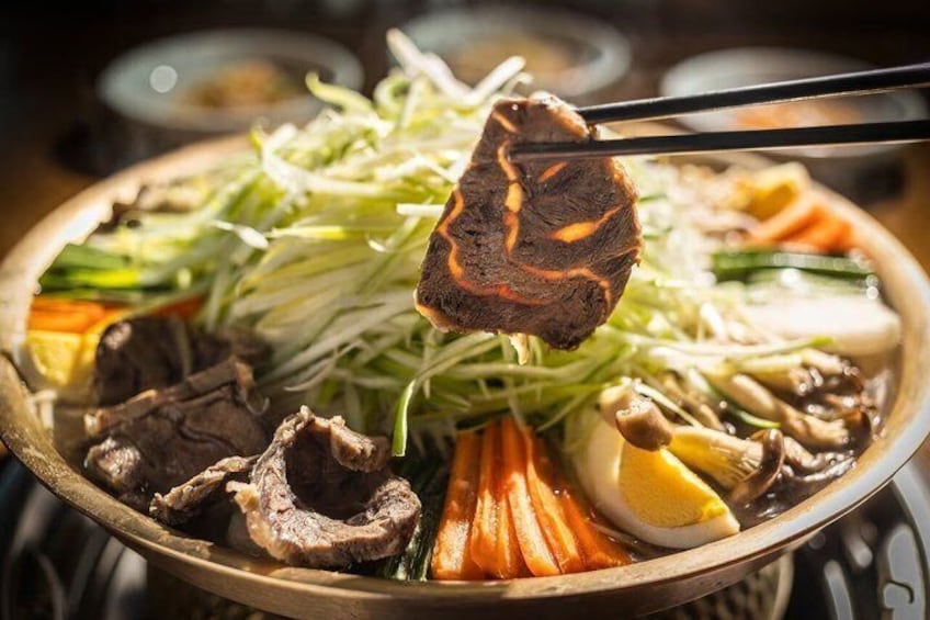 A hot pot with various meats, vegetables, and a piece of meat being held by chopsticks. 5