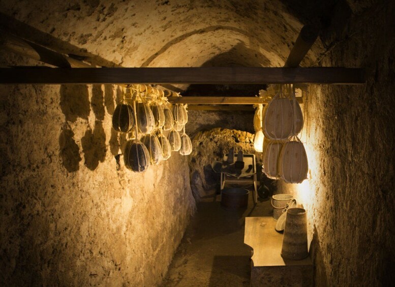 A dimly lit underground cellar with wooden beams, stone walls, and various containers hanging from the ceiling. 5