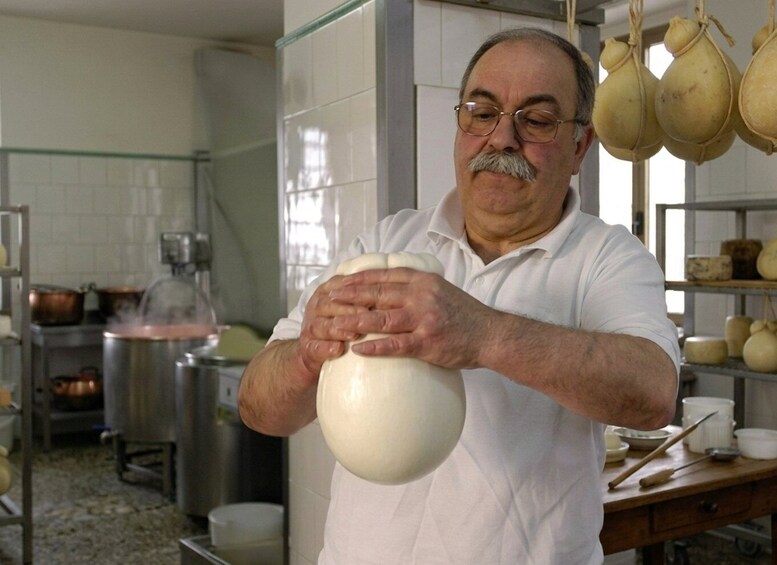 A person kneading dough in a kitchen with cooking equipment and hanging gourds in the background. 4