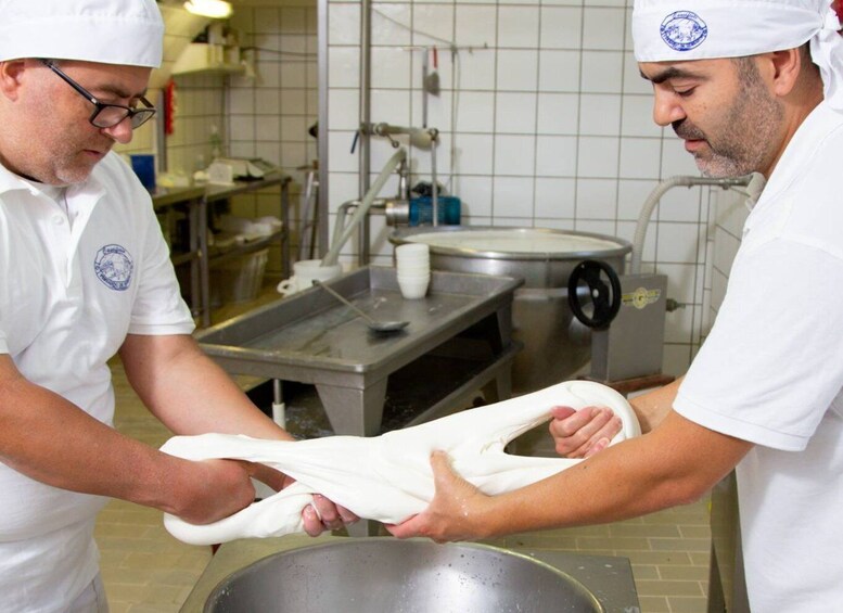 Two individuals in a kitchen, one stretching dough. 1