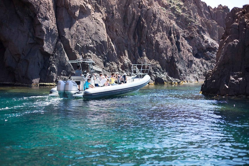 A boat with passengers on a clear turquoise sea, surrounded by rocky cliffs. 1