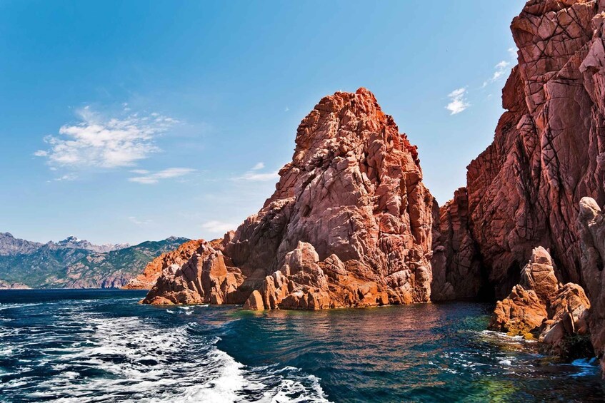 A coastal rock formation with clear blue waters and distant mountains. 4