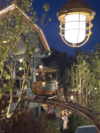 A vintage tram at night, illuminated by a large hanging lamp, with trees and a building in the background. 3