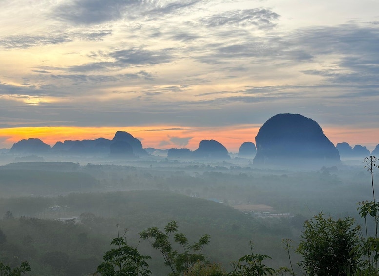 A landscape with a large rock formation silhouetted against a sunset sky. 1