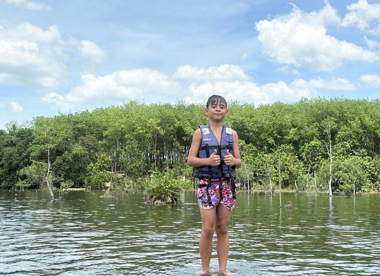 A person standing in water with a life jacket, surrounded by dense greenery and trees. 5