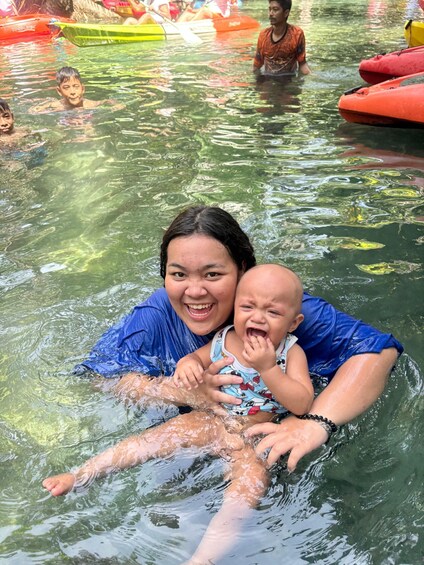 A woman and a baby in a body of water with inflatable boats in the background. 3